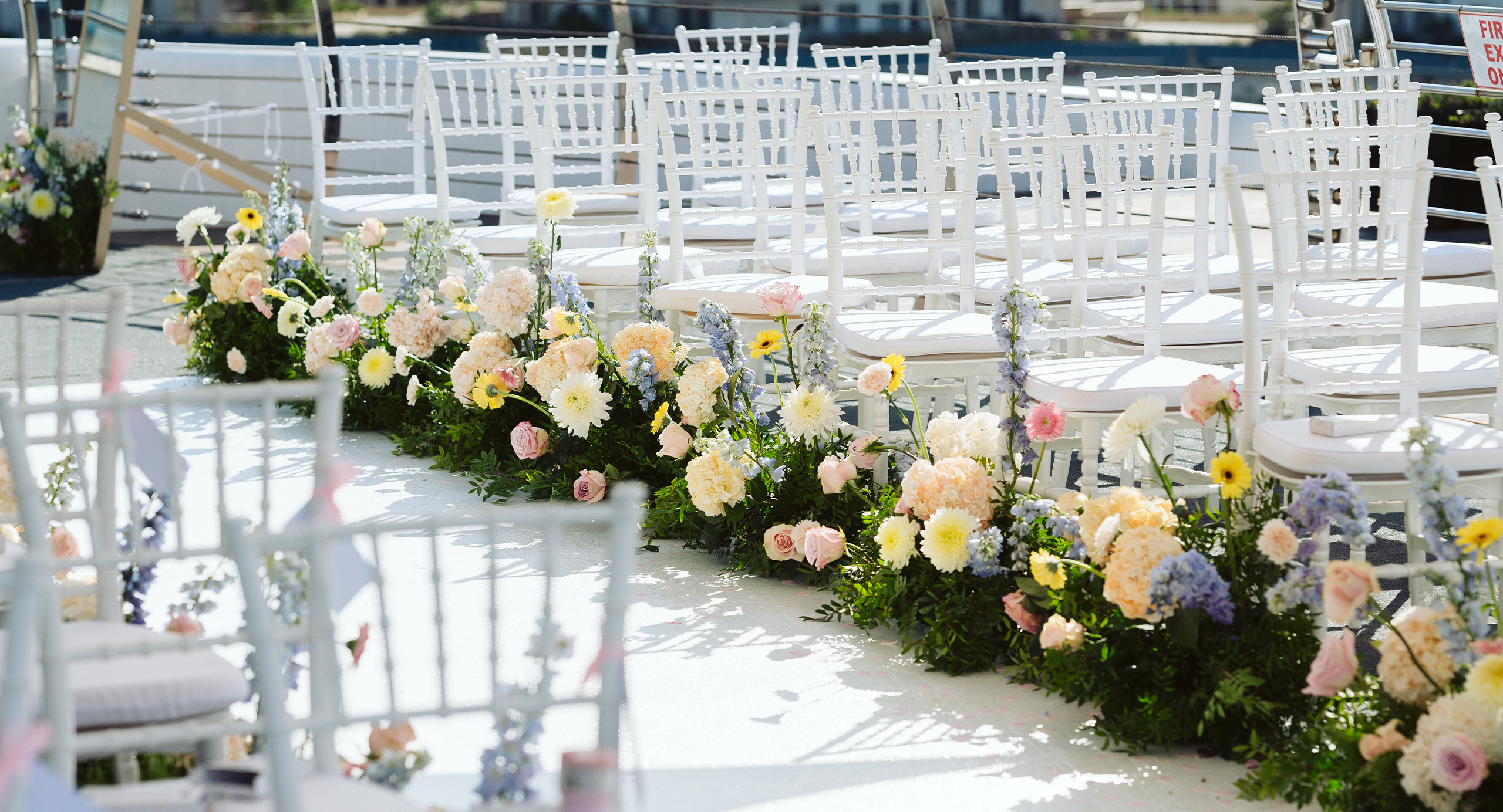 Rows of white chairs arranged outdoors with floral decorations lining the aisle for a wedding ceremony.