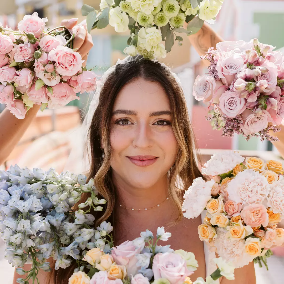A woman smiles at the camera while surrounded by bouquets of various colorful flowers held around her head and shoulders.