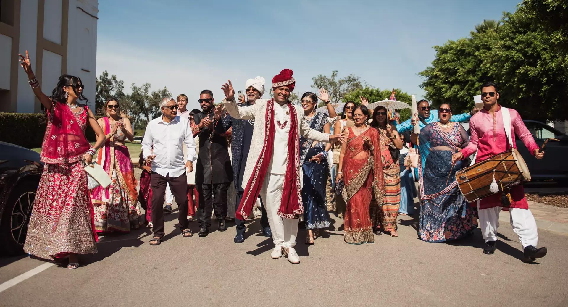 A groom in traditional Indian attire dances with a group of guests outdoors during a wedding celebration, with people smiling and wearing colorful clothing.