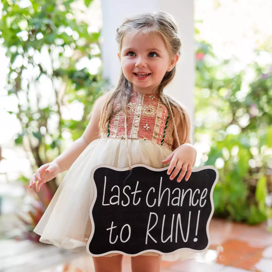 Young girl in a decorative dress stands outside holding a sign that reads 