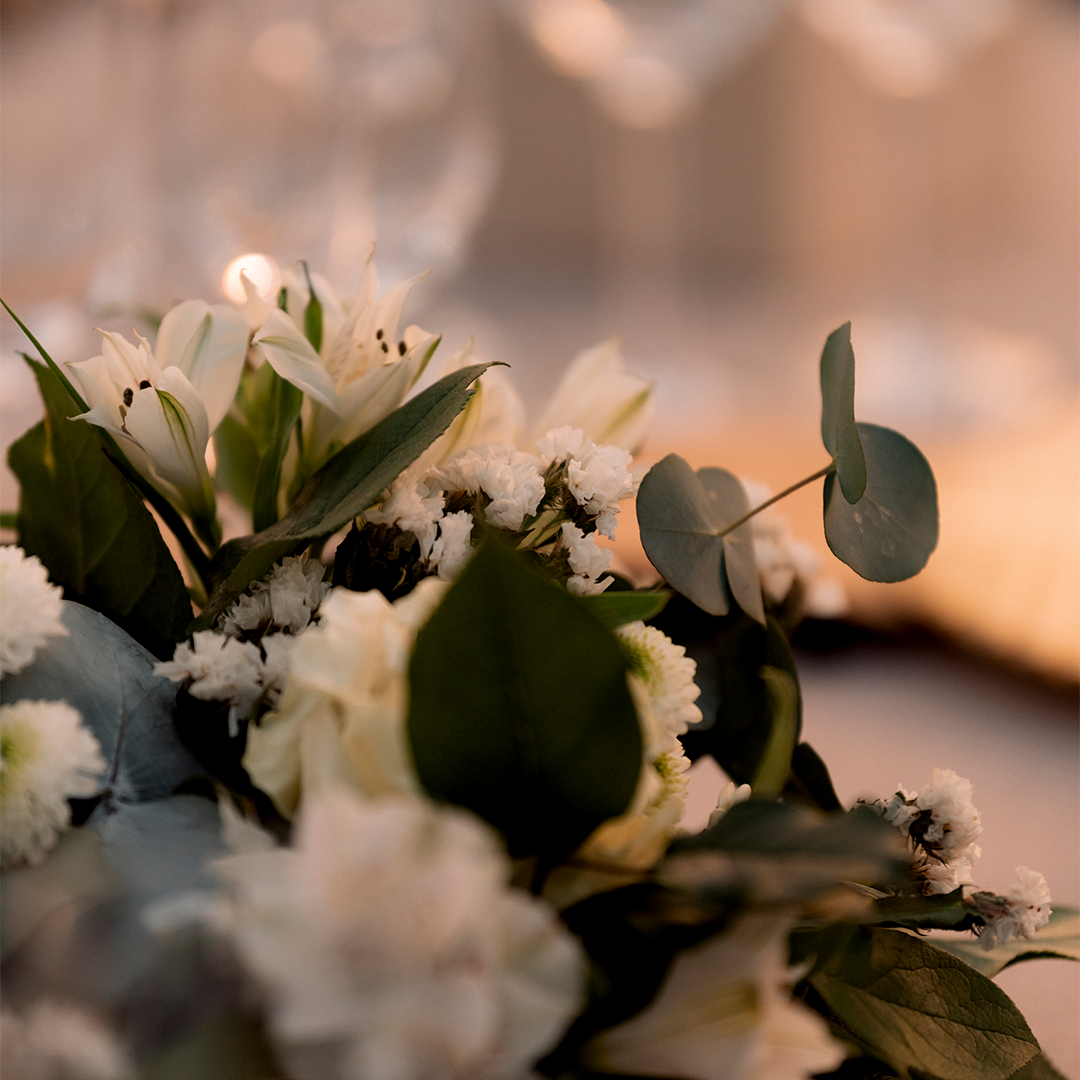 Close-up of a floral arrangement featuring white flowers, green leaves, and eucalyptus, with a softly blurred background.