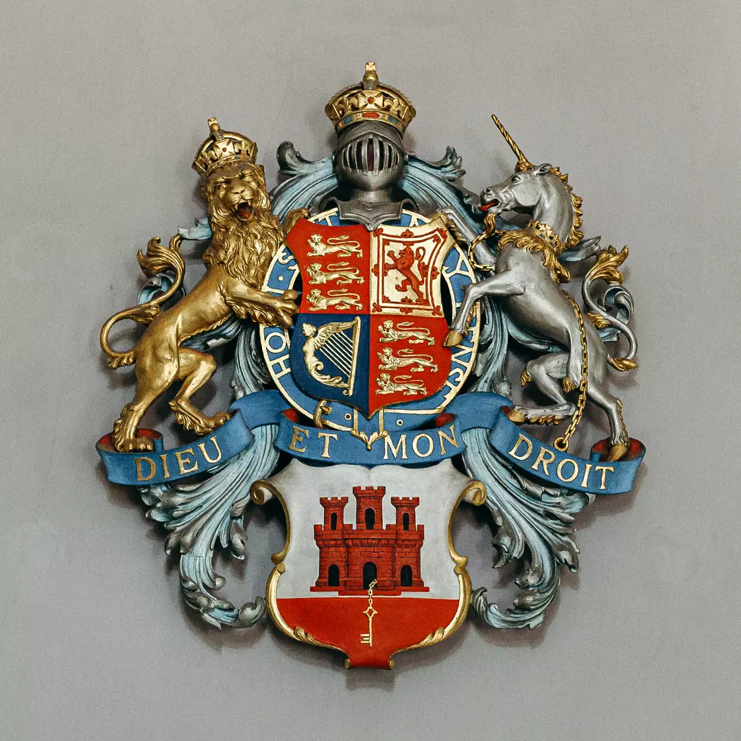 A royal coat of arms featuring a crowned lion, a unicorn, a shield with symbols, and a banner reading 
