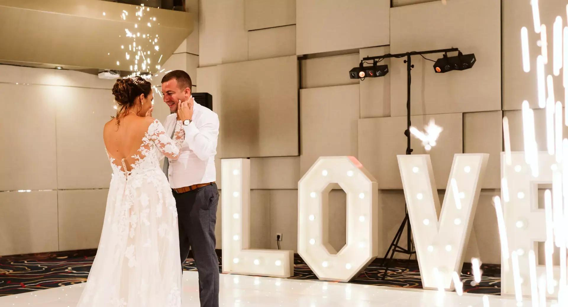 Bride and groom share a first dance on a lit dance floor with large illuminated letters spelling 