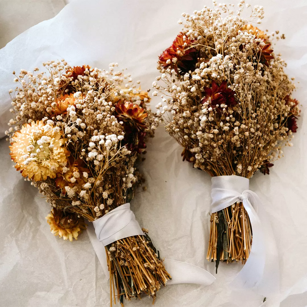 Two small bouquets of dried flowers with white ribbons wrapped around the stems are placed on white tissue paper.