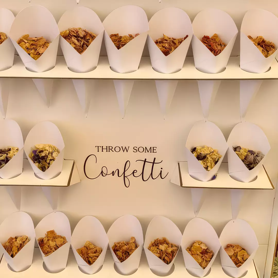 White paper cones filled with dried flower petals are arranged on two shelves, with the words 